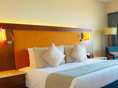 Nowoczesny pokój hotelowy z dużym łóżkiem, drewnianym zagłówkiem i miękkim oświetleniem.