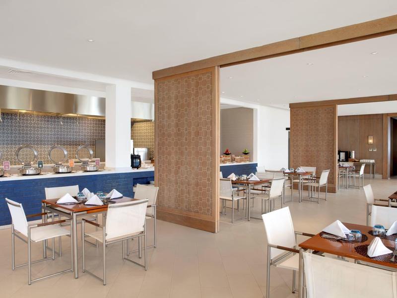 Nowoczesna jadalnia z drewnianymi stolikami i białymi krzesłami w jasnej, otwartej przestrzeni.