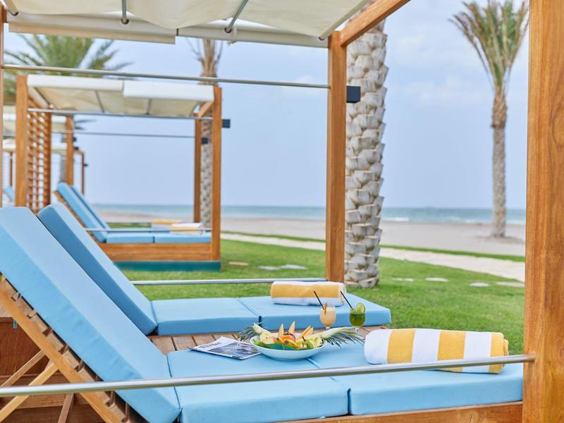 Niebieskie leżaki z kocami pod drewnianymi pergolami na plaży z widokiem na morze.