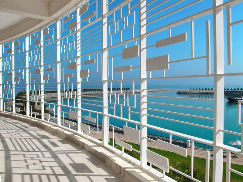 Widok na morze przez geometryczną białą metalową balustradę na balkonie hotelowym.