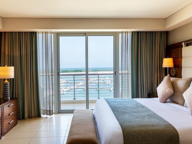 Jasny pokój hotelowy z dużym łóżkiem, balkonem i widokiem na morze.