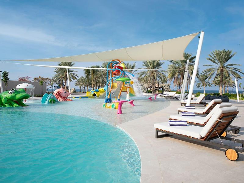 Strefa basenowa z leżakami i zacienionym placem zabaw z zjeżdżalniami wodnymi