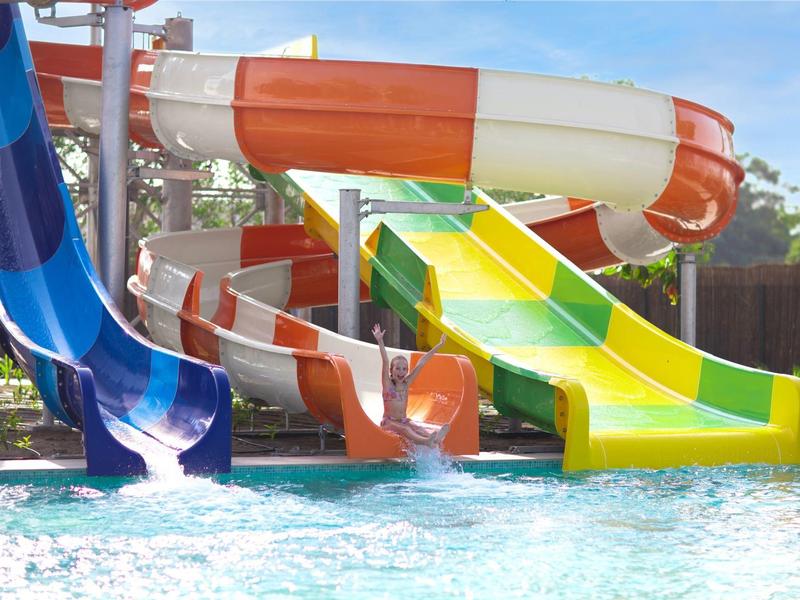 Kilka kolorowych zjeżdżalni wodnych prowadzi do basenu pod jasnym niebem.