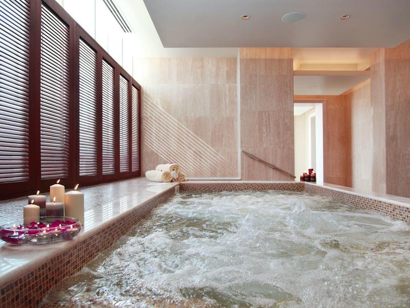 Wanna z hydromasażem w pomieszczeniu z bulgoczącą wodą, świecami i płatkami w nowoczesnym spa.