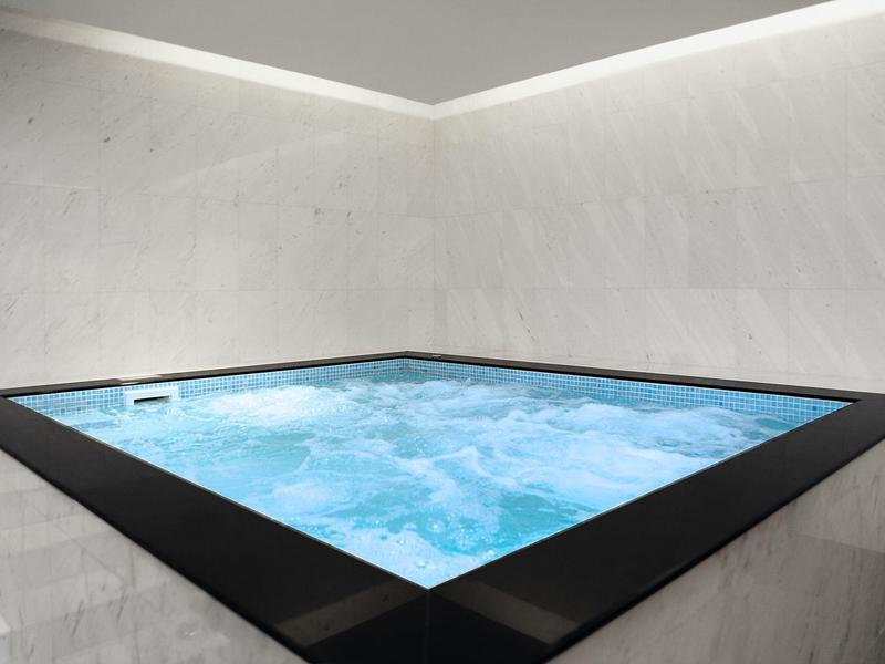 Nowoczesne jacuzzi z bulgoczącą wodą w minimalistycznym pomieszczeniu z szarymi ścianami.