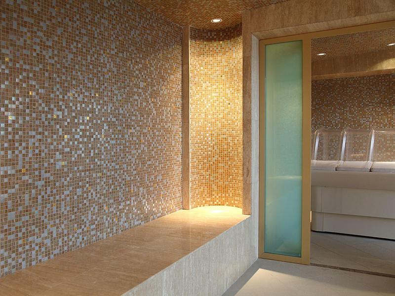 Nowoczesna strefa wellness z mozaikowymi ścianami i sauną z przeszklonymi drzwiami