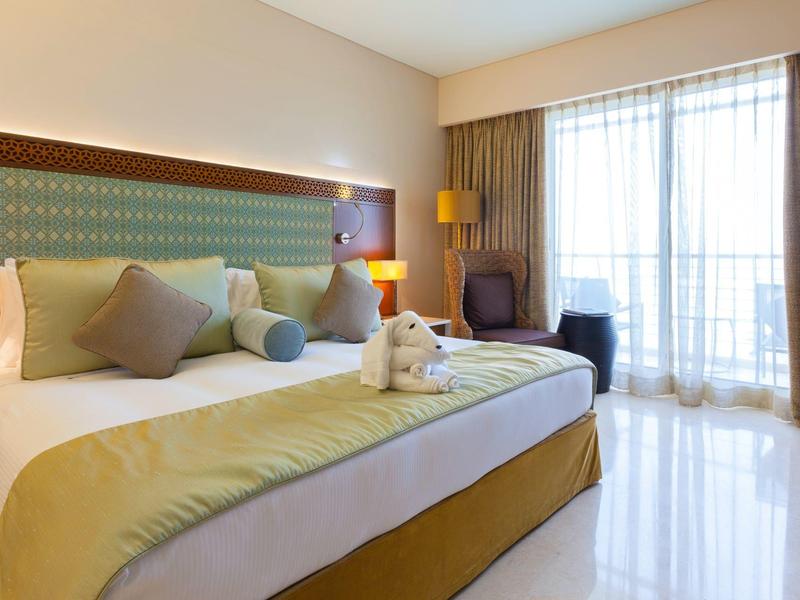 Nowoczesny pokój hotelowy z dużym łóżkiem, częścią wypoczynkową i balkonem z dostępem do światła dziennego.