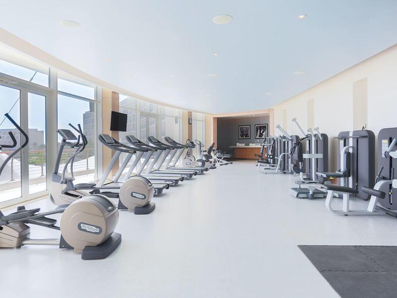 Jasna, nowoczesna siłownia z bieżniami, orbitrekami i maszynami siłowymi w przestronnym pomieszczeniu.