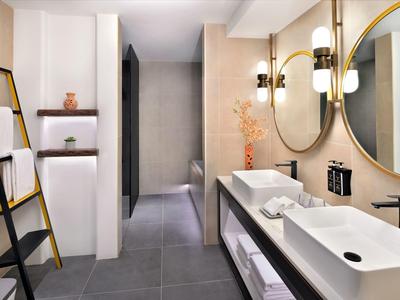 Moderní hotelová koupelna s dvojitým umyvadlem, kulatým zrcadlem a stylovým osvětlením.