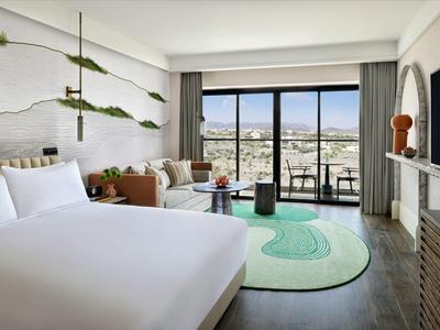 Moderní hotelový pokoj s velkou postelí, pohovkou, kobercem a balkonem s výhledem na město.