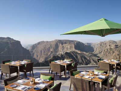 Terasa s prostřenými stoly a zeleným slunečníkem před horskou krajinou