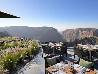 Terrassengarten mit Tischen und Stühlen, umgeben von Bergen und Pflanzen unter klarem Himmel.