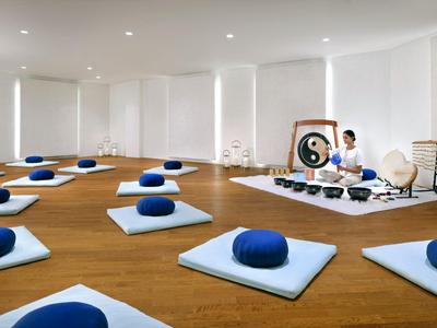 Großer, heller Raum mit Meditationskissen und Person vor Gong für Yoga oder Meditation.