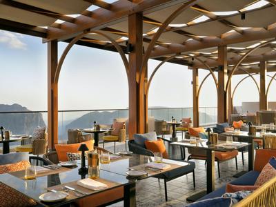 Terrasse eines Hotels mit Holzgitterdach, gedeckten Tischen und Blick auf das Meer.