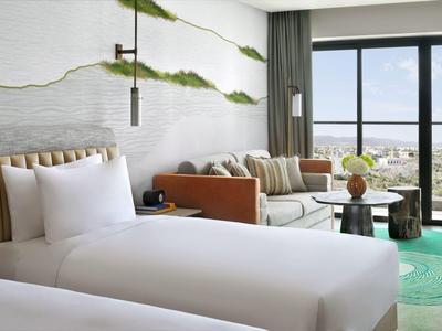 Světle zařízený hotelový pokoj se dvěma jednolůžky a výhledem na moře přes velká okna.