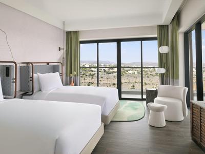 Moderní hotelový pokoj se dvěma postelemi a velkým oknem s výhledem na město.