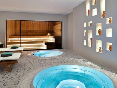 Moderní spa s modrými vířivkami, dřevěnými lavicemi a dekorativními nikami ve zdi.