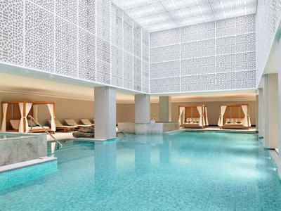 Luxusní vnitřní bazén s lehátky a pohodlnými sezeními obklopený elegantními bílými zdmi.