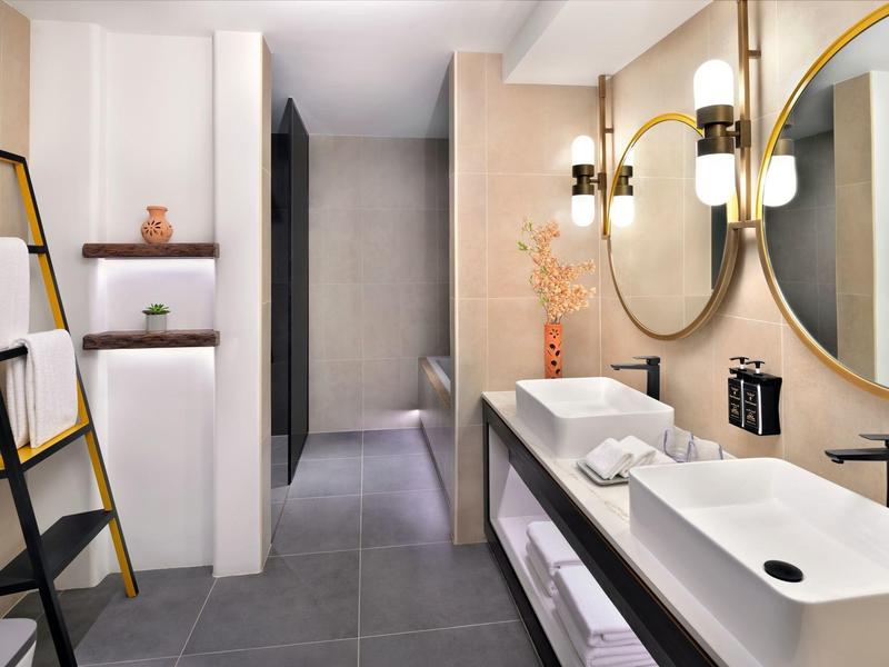 Moderní hotelová koupelna s dvojitým umyvadlem, kulatým zrcadlem a stylovým osvětlením.