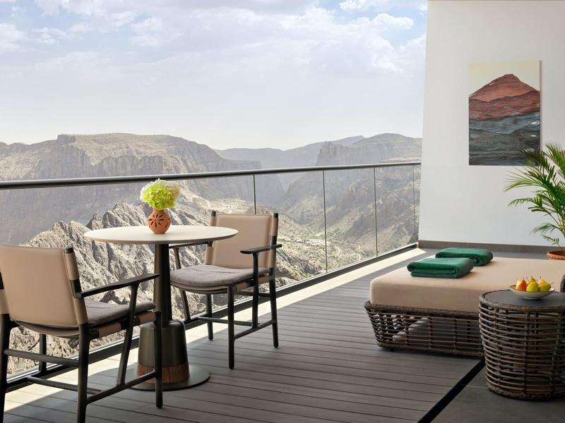 Balkon s stolem, židlemi a lehátkem s výhledem na horskou krajinu při zatažené obloze.