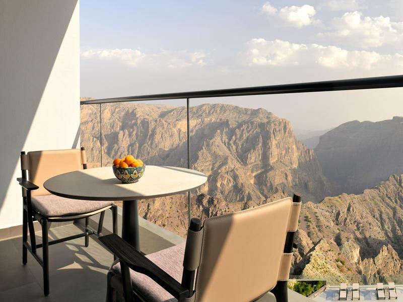 Balkon s stolem a židlemi s výhledem na skalnaté hory při západu slunce.