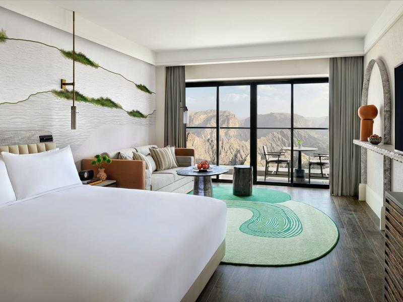 Moderní hotelový pokoj s velkou postelí, posezením a balkonem s výhledem na hory.