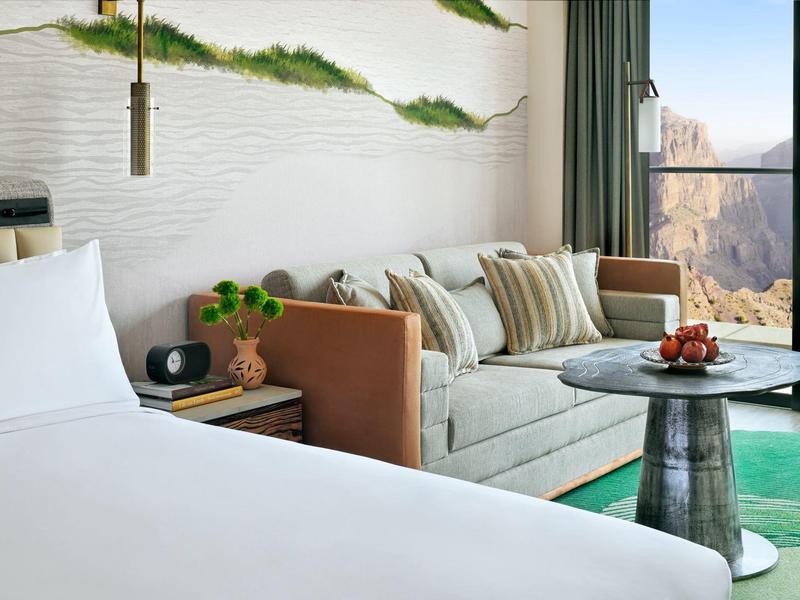 Moderní hotelový pokoj s velkou postelí, pohovkou a panoramatickým výhledem na hory.