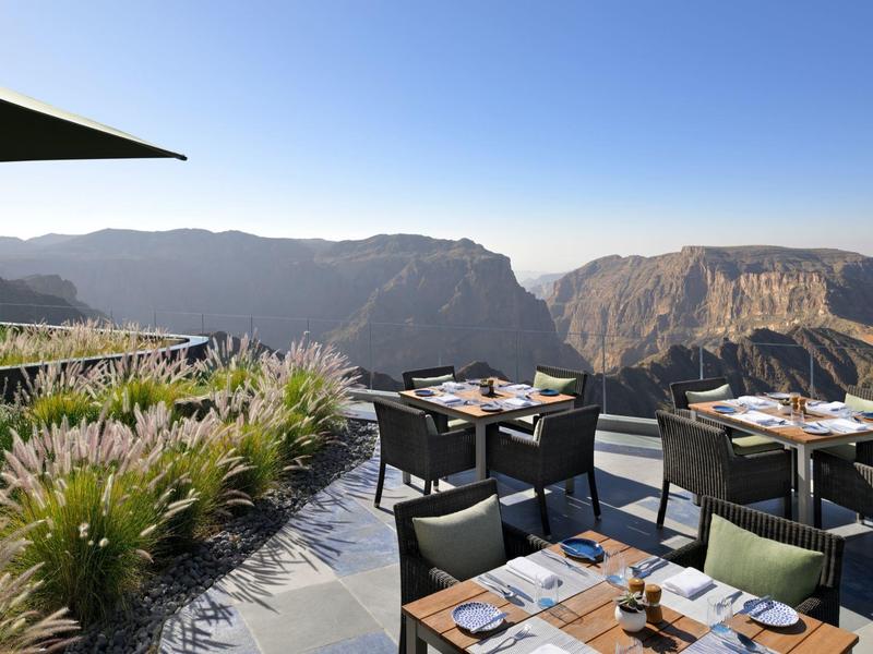 Terasa s prostřenými stoly a židlemi s výhledem na horskou krajinu za jasné oblohy.