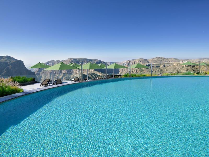 Velký infinity bazén s výhledem na horskou krajinu a jasnou modrou oblohu.