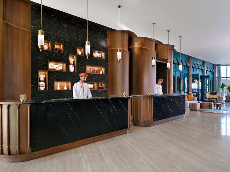 Moderní hotelová recepce se dvěma zaměstnanci za černým mramorovým pultem.