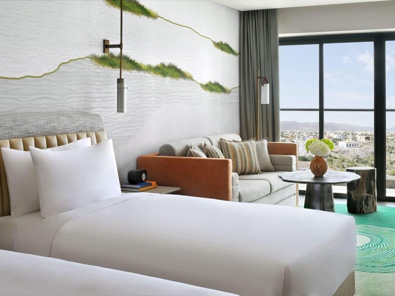 Světle zařízený hotelový pokoj se dvěma jednolůžky a výhledem na moře přes velká okna.