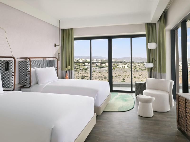 Moderní hotelový pokoj se dvěma postelemi a velkým oknem s výhledem na město.