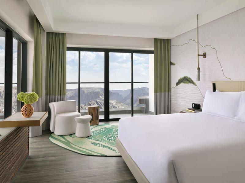 Světý hotelový pokoj s velkou postelí, posezením a panoramatickým výhledem na hory.