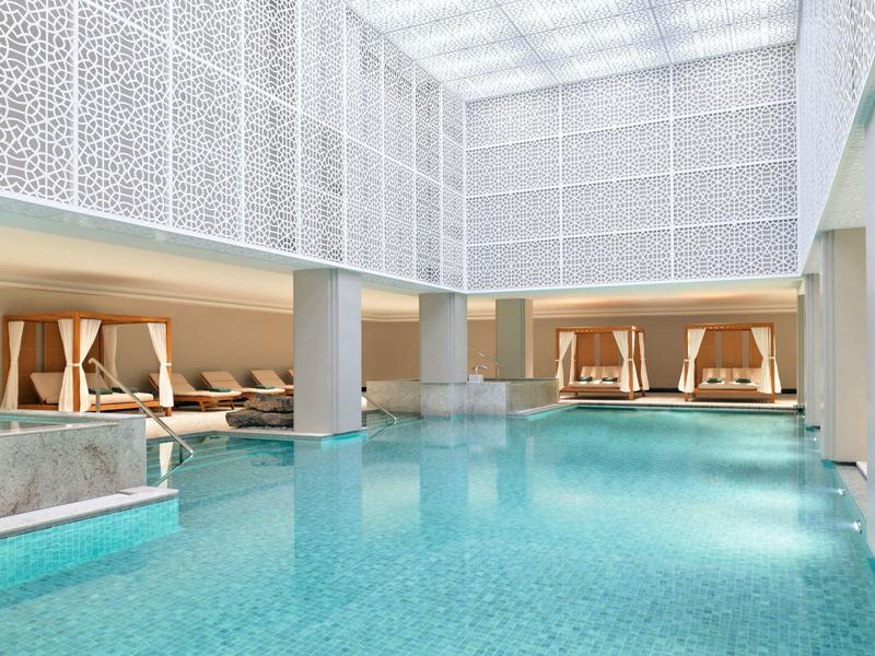 Luxusní vnitřní bazén s lehátky a pohodlnými sezeními obklopený elegantními bílými zdmi.