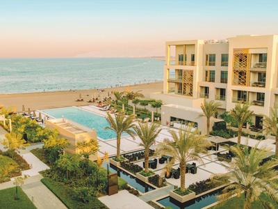 Hotelcomplex met zwembad en palmbomen aan zee bij zonsondergang