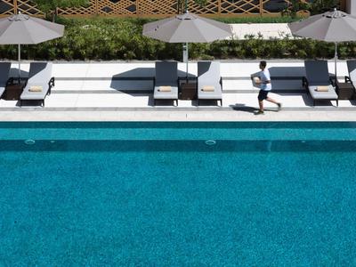 Vogelperspektive auf einen blauen Pool mit Liegestühlen und Sonnenschirmen am Rand.