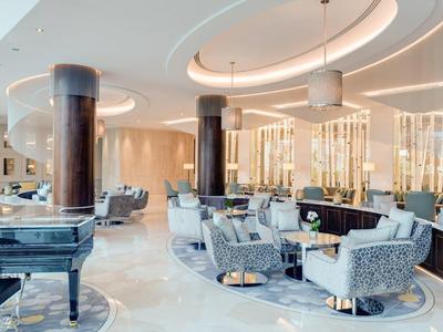 Luxe hotel lobby met moderne zitgedeeltes, piano en gebogen plafond elementen.