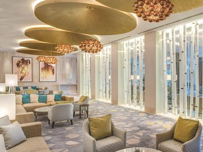 Moderne hotel-lounge met grote ramen, comfortabele fauteuils en opvallende plafondlampen.