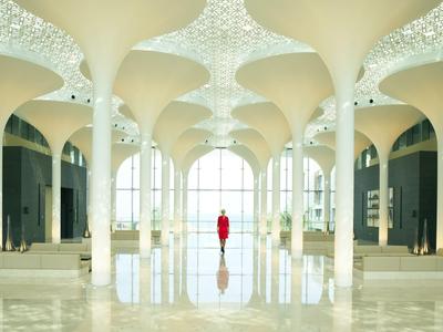 Helle, moderne Hotellobby mit hohen Gewölbedecken und einer Person in roter Kleidung.