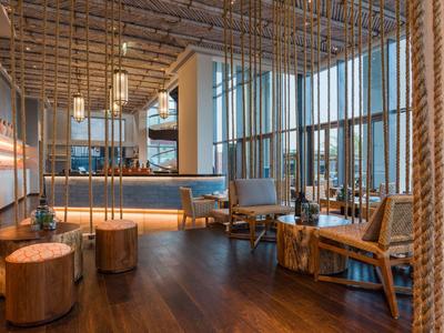 Moderne hotel lounge met hout- en touwelementen, fauteuils en grote ramen.