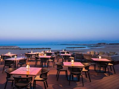 Buitenrestaurant met verlichte tafels op terras bij het strand bij zonsondergang.