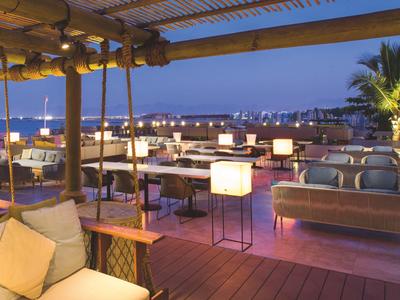 Avondterras van hotel met loungebanken en verlichte tafels onder open hemel.