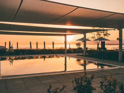 Poolbereich mit Blick auf das Meer bei Sonnenuntergang, gedeckt von einem Pavillon.