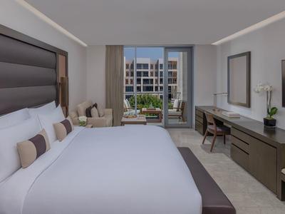 Moderne hotelkamer met groot bed, bureau en uitzicht op het zwembadgebied.