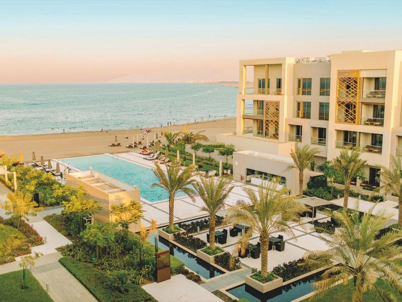 Hotelcomplex met zwembad en palmbomen aan zee bij zonsondergang