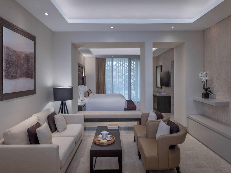 Moderne hotelkamer met bank, fauteuils, bed en grote tv in neutrale kleuren.