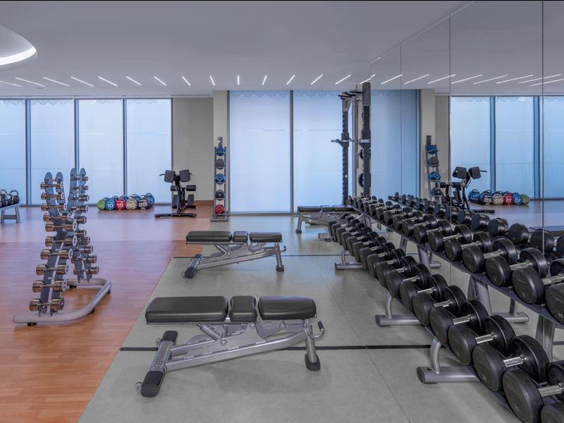 Moderne fitnessruimte met losse gewichten, banken en grote ramen met uitzicht naar buiten.