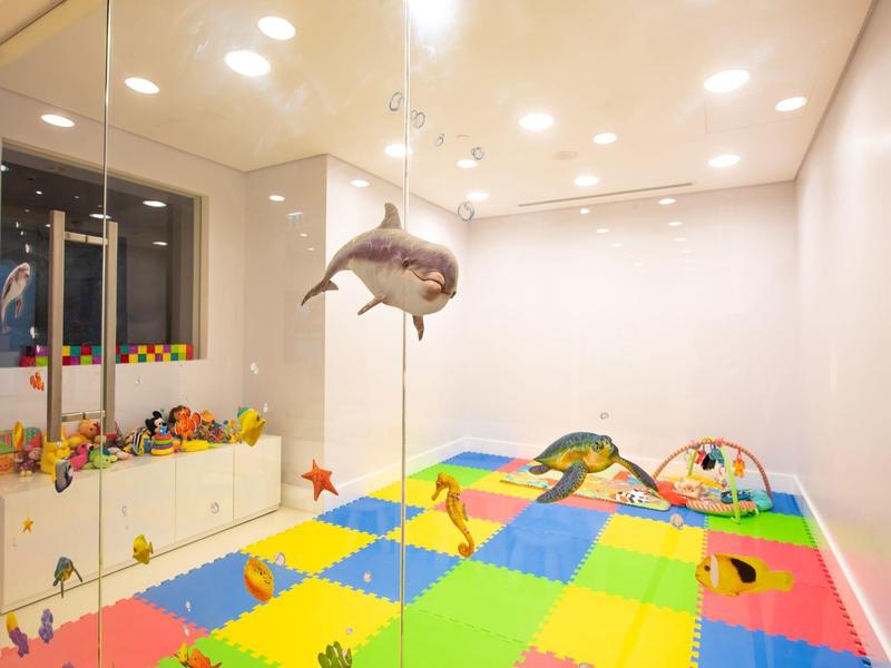 Kleurrijke speelkamer met zachte vloer, speelgoed en een hangende haai decoratie.