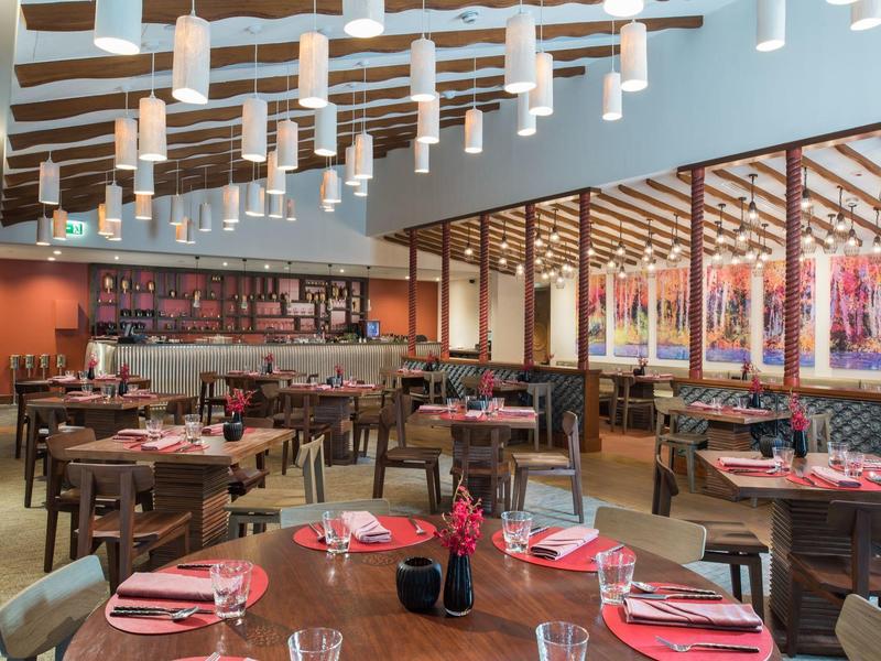 Modern restaurant met houten balkenplafond, ronde tafels en grote raamwand