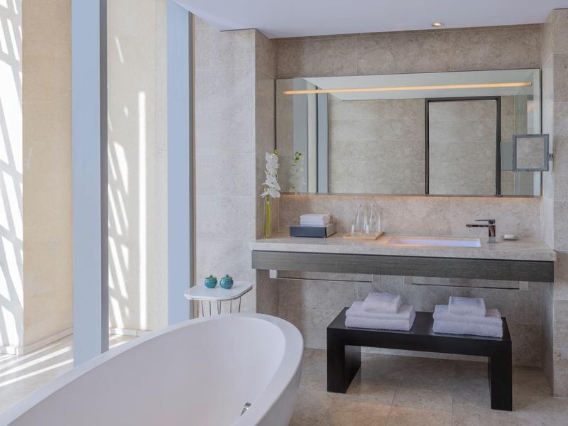 Lichte badkamer met vrijstaand bad, wasbak en grote spiegel.